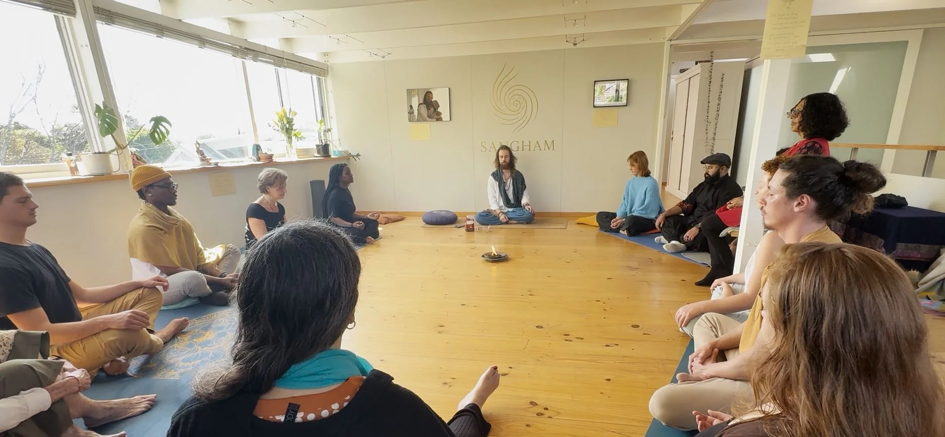 A Sangham group sitting in a circle in a light-filled room in Cape Town, with the facilitator seated at the head of the circle